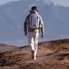 MAN WALKING IN DESERT WITH WHITE BACKPACK