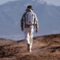 MAN WALKING IN DESERT WITH WHITE BACKPACK
