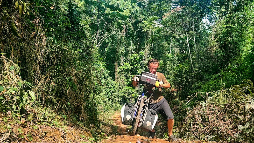 Explorer Jude Kriwald pushing his bike up a dusty track in the Gola Rainforest
